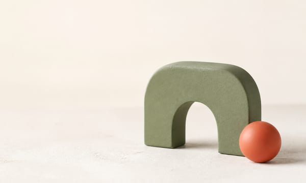 An olive-green arch and a coral sphere arranged on a cream surface